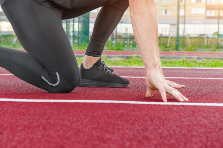 Athlete on the starting line of a stadium track preparing for a run. Young muscular athlete is at...