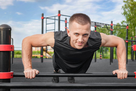 Young man doing push-up exercise on the street on an iron bar.