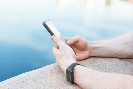 Close-up hands. Male hand pressing button menu on smart watch checking heart rate on monitor after jogging in the park. Smart watch and phone in hands close-upの写真素材