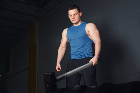 The guy performs an exercise with a sledgehammer for training.