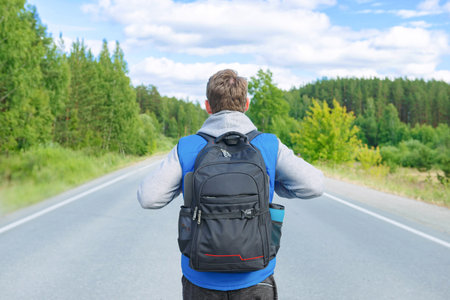 A man in a blue tank top and gray turtleneck is walking along the road with a backpack.の写真素材