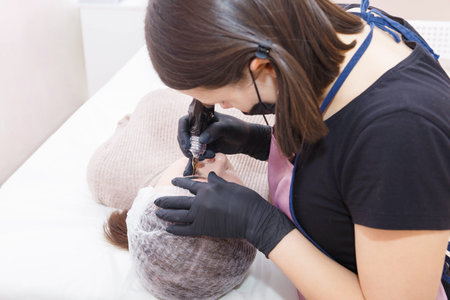The master applies eyebrow makeup paint to the client with a tattoo machine.の写真素材