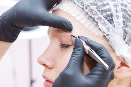 The master removes tweezers with eyebrow hair after the procedure.