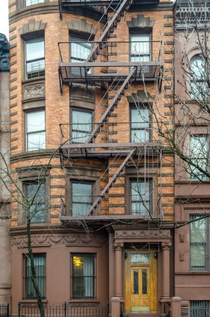 Typical New York City Apartment Building with Fire Escape Ladders and Yellow Wooden Door at the Entrance. New York City, USAのeditorial素材