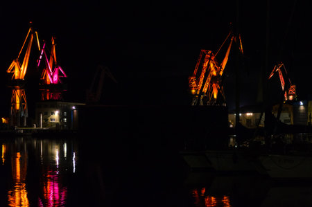 Large Illuminated Cranes at the Pula Shipyard in Croatia at Night. Colors Reflect on the Dark Waters at the Port. LED Light Choreography.の写真素材
