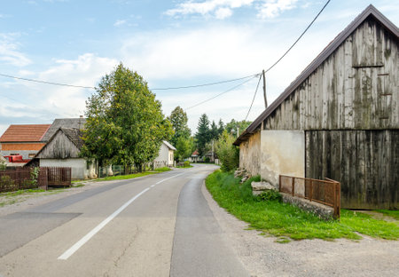 Driving on a Provincial Road through Villages in Croatian Countryside. Rural Scenery with Green Trees and Old Cottages on a Sunny Day.の写真素材