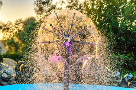 Beautiful Round Fountain Bursting Water Droplets in a Pattern. Wind Blows the Waters Away. Sunset Creates nice Colors.の写真素材