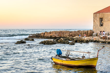 Traditional Yellow Fishing Boat in Chania City at the Greek Island of Crete during Sunset. Wild Rocky Bay in Summer Season in Greece. Beautiful Sky Colors in the Horizon.の写真素材