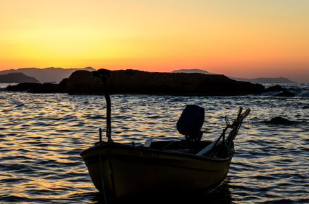 Silhouette of a Traditional Yellow Fishing Boat in the Greek Island of Crete at Sunset. Summer Season in Greece. Beautiful Sky Colors.の写真素材