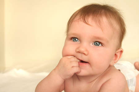 baby lying on tummy on white bed sheets chewing his/her fingersの写真素材