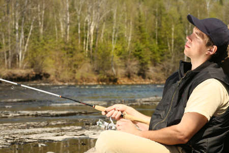 a really relaxed looking fisherman sitting on the rocks by the riverの写真素材