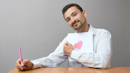 A man in a white shirt is holding a drawing. a person draws a heart shapeの写真素材