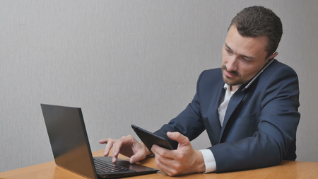 A man checks the information on three devices at once. The person is shopping online and talking on the phone. He works on the Internet. businessman with the phone Tablet and laptopの写真素材
