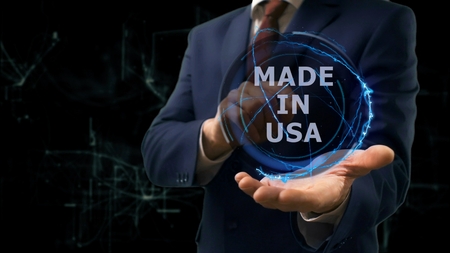 Businessman shows concept hologram Made in USA on his hand. Man in business suit with future technology screen and modern cosmic backgroundの写真素材