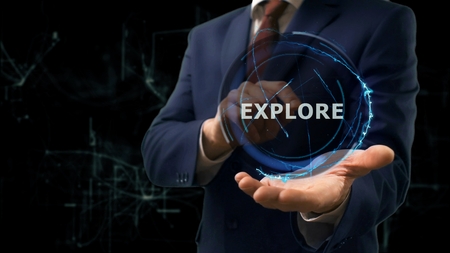 Businessman shows concept hologram Explore on his hand. Man in business suit with future technology screen and modern cosmic backgroundの写真素材
