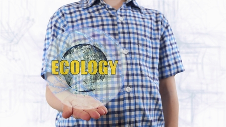 Young man shows a hologram of the planet Earth and text Ecology. Boy with future technology 3d projection on a modern white digital backgroundの写真素材