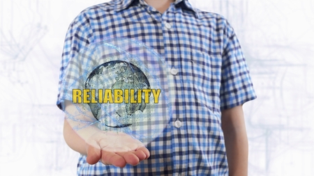 Young man shows a hologram of the planet Earth and text Reliability. Boy with future technology 3d projection on a modern white digital backgroundの写真素材