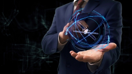 Businessman shows concept hologram 3d Satellite on his hand. Man in business suit with future technology screen and modern cosmic backgroundの写真素材