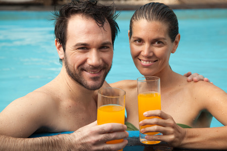 Couple in love drinking orange juice on the edge of the poolの写真素材