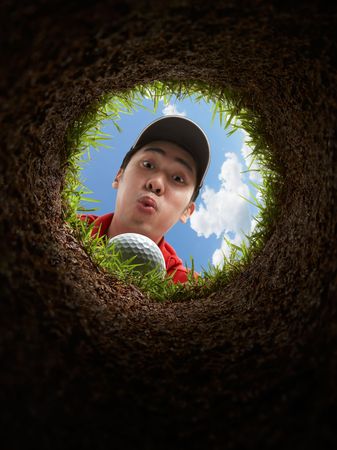 golfer blowing golf ball, view from inside the holeの写真素材