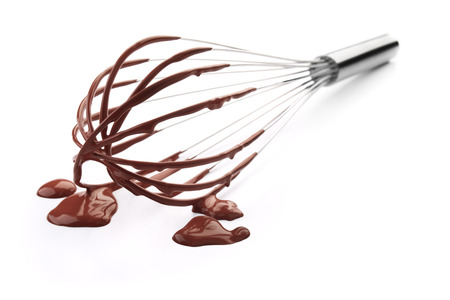 wire whisk with chocolate against white backgroundの写真素材