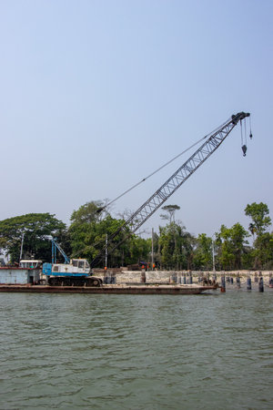 Large water crane on a river. Industrial riverbank with a water crane and beautiful nature. Riverbank full of concrete pillars. Beautiful southeast Asian river and blue sky shot. Coast of a river.の写真素材