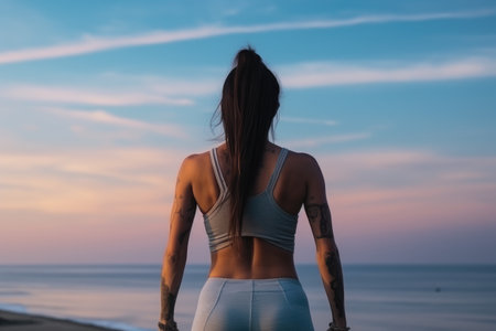 Back view of a young woman in sportswear standing on the beach at sunset, Back view of woman athlete in sportswear doing stretching and warm up for hands outdoors on ocean beach, AI Generatedの素材