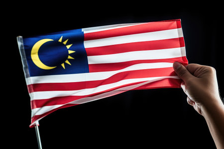 A man holding a Malaysia flag in front of a black background, Hand waving the Malaysia flag, also known as Jalur Gemilang, in conjunction, AI Generatedの素材