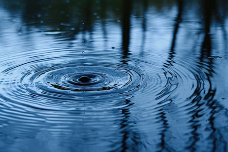 A single water drop falls from a leaf, captured against a backdrop of trees, Raindrop hitting the surface of a calm pond, AI Generatedの素材