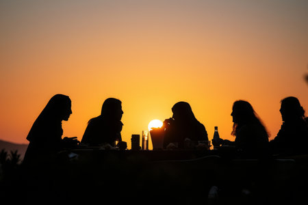 A diverse group of individuals sitting and conversing around a table as the sun sets in the background, Sunset silhouette of friends at an iftar, AI Generatedの素材