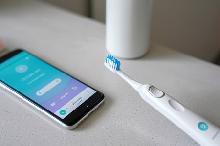 A smart phone and a toothbrush placed side by side on a table, Smart toothbrush connected to a dental health app, AI Generatedの素材