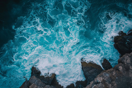 This aerial photograph captures a body of water bordered by rocks, showcasing the natural elements of the scene, Striking aerial perspective of a ocean wave hitting the rocks, AI Generatedの素材