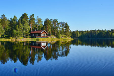 A house perched on the shore of a calm lake under a clear blue sky, A peaceful lakeside retreat, with a clear blue sky reflected in the waterの素材