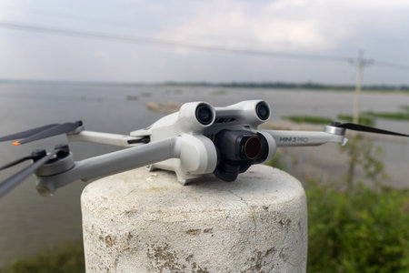 A compact drone perched on a concrete post near a river, ready for aerial photography during golden...