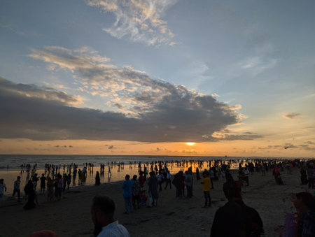 Crowds gathering at a beach during sunset with colorful skies and reflected water creating a serene atmosphere for evening relaxationの写真素材