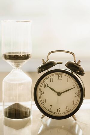 Vintage alarm clock And hourglass In the very bright light from behindの写真素材