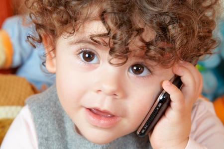 Two year old girl with curly hair talking on phone.の写真素材