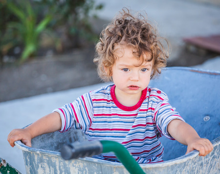 Portrait of 1 year old baby boy playing with a wheel barrow.の写真素材