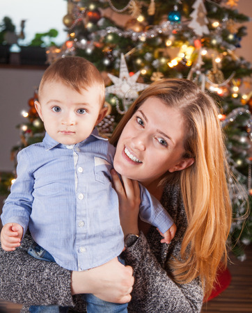 1 year old baby boy in his mother's arms, near the Christmas tree.の写真素材