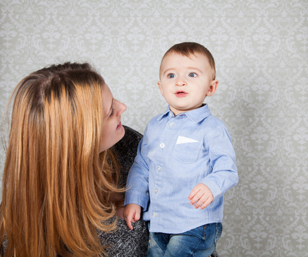 1 year old baby boy in his mother's arms, studio portrait.の写真素材