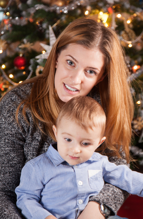 1 year old baby boy in his mother's arms, near the Christmas tree.の写真素材