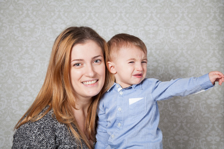 1 year old baby boy in his mother's arms, studio portrait.の写真素材