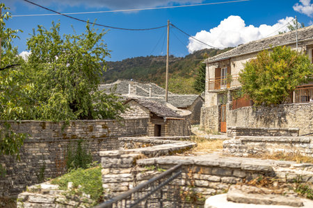 Picturesque view of Monodendri village in Zagori, Epirus, Greece, on a sunny yet cloudy autumn day. The scene showcases traditional stone houses, vibrant fall foliage, and the stunning mountainous landscape of the region. A perfect representation of Greeceâs rural charm and natural beauty, ideal for travel and landscape photography.の写真素材