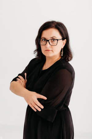 Studio portrait of a confident 40-year-old woman wearing an elegant black outfit and glasses against a clean white background. She exudes professionalism and sophistication, making the image ideal for business, corporate, fashion, and lifestyle concepts. Perfect for marketing, editorial, and commercial use.の写真素材