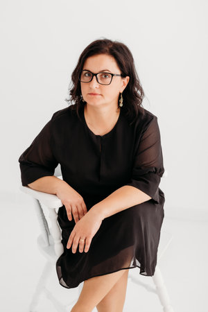Studio portrait of a confident 40-year-old woman wearing an elegant black outfit and glasses against a clean white background. She exudes professionalism and sophistication, making the image ideal for business, corporate, fashion, and lifestyle concepts. Perfect for marketing, editorial, and commercial use.の写真素材