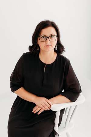 Studio portrait of a confident 40-year-old woman wearing an elegant black outfit and glasses against a clean white background. She exudes professionalism and sophistication, making the image ideal for business, corporate, fashion, and lifestyle concepts. Perfect for marketing, editorial, and commercial use.の写真素材