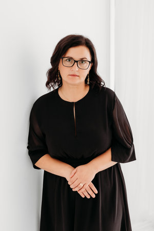 Studio portrait of a confident 40-year-old woman wearing an elegant black outfit and glasses against a clean white background. She exudes professionalism and sophistication, making the image ideal for business, corporate, fashion, and lifestyle concepts. Perfect for marketing, editorial, and commercial use.の写真素材