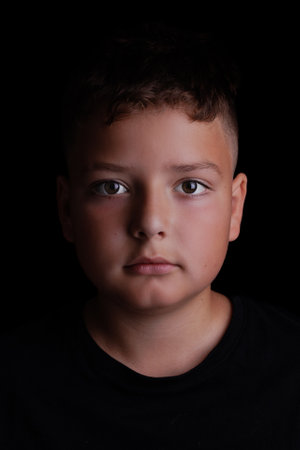 Studio portrait of a 10-year-old preteen boy against a black background.の写真素材