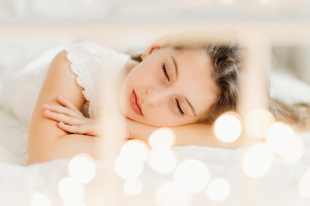 Studio portrait of a delicate 10-year-old girl in a festive Christmas setting. Surrounded by warm lights and holiday decorations, she exudes innocence and joy, capturing the magic of the season.の写真素材