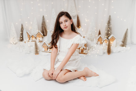 Studio portrait of a delicate 10-year-old girl in a festive Christmas setting. Surrounded by warm lights and holiday decorations, she exudes innocence and joy, capturing the magic of the season.の写真素材